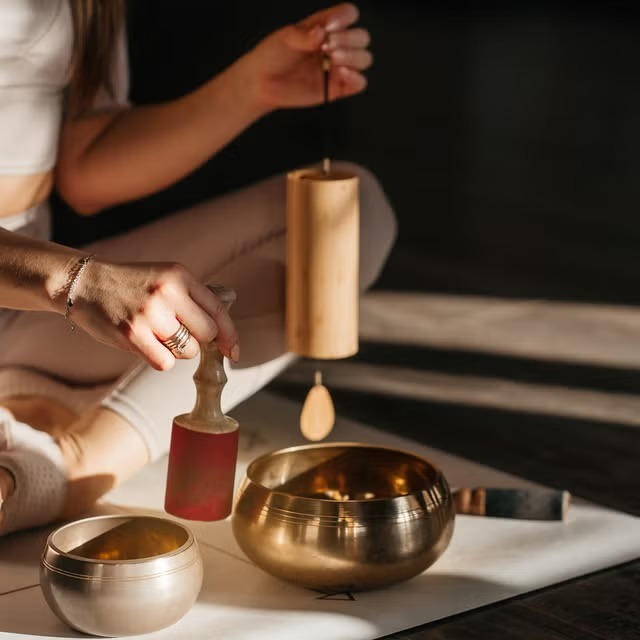 Sound practitioner with bamboo Koshi chime and resonant singing bowl in warm light